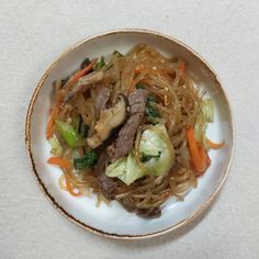 a white plate topped with meat and veggies covered in broccoli noodles