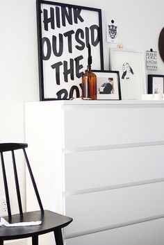 a white dresser sitting next to a black chair in a room with pictures on the wall