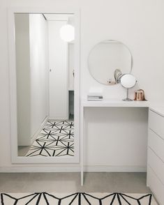 a white bathroom with a black and white rug on the floor next to a mirror