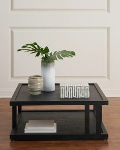 a black coffee table with a plant on top and stacks of books in the middle