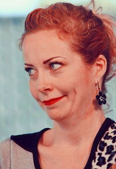 a woman with red hair and blue eyes smiles at the camera while wearing black earrings