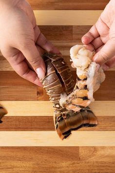 two hands are grabbing food from a piece of wood on a wooden table with another hand reaching for it