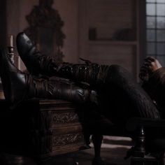 a woman sitting on top of a wooden bench in a dark room with her legs crossed