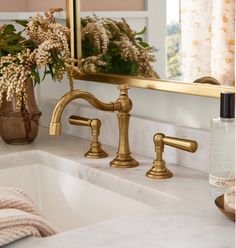 a bathroom sink with gold faucets and flowers in the mirror above it,