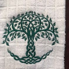 an embroidered tree of life on a white towel with green leaves and vines in the center