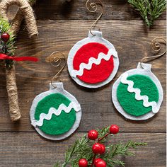 three christmas ornaments on a wooden table next to some branches and red balls with green trim