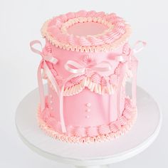 a pink and white cake with bows on top sitting on a table in front of a white backdrop