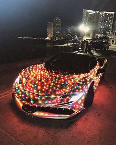 a car covered in christmas lights parked on the side of the road near a city at night