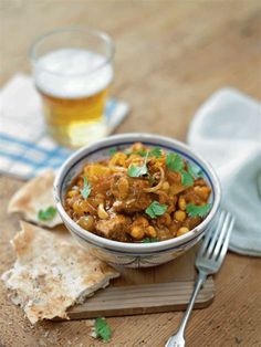 a bowl filled with food sitting on top of a wooden cutting board next to a glass of beer