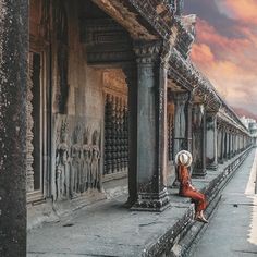 a woman sitting on the side of a building next to a body of water at sunset