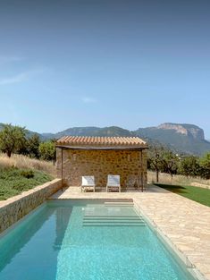 an empty swimming pool in front of a stone building with mountains in the background and grass on either side