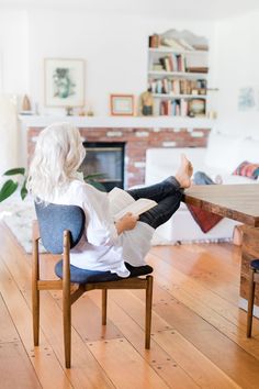 a woman sitting in a chair with her feet up on the table and reading a book