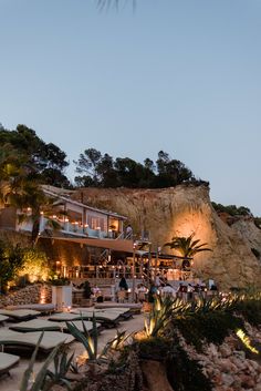 an outdoor dining area at dusk with people sitting and standing on the patio, surrounded by greenery