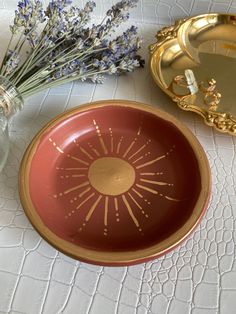 a red and gold plate sitting on top of a table next to a vase filled with flowers