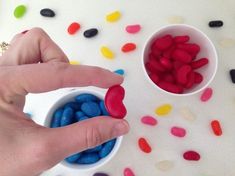 a person is holding some candy in their hand next to two small bowls filled with jelly beans