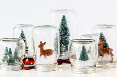 snow globes with christmas trees and deer in them are sitting on a white surface