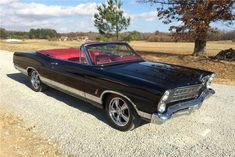 an old black car is parked on the gravel