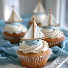 some cupcakes with white frosting and sailboats on top are sitting on a plate