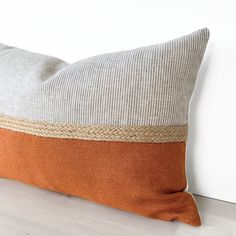 an orange and grey pillow sitting on top of a wooden floor next to a white wall