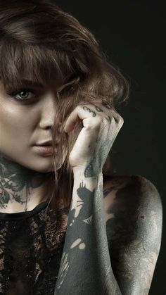 a woman with tattoos on her arm and shoulder posing for a photo in front of a black background