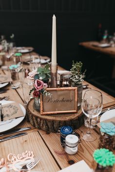 a wooden table topped with lots of plates and place settings next to a tall candle