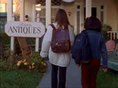 two people are walking down the sidewalk towards an antique store with a clock on it