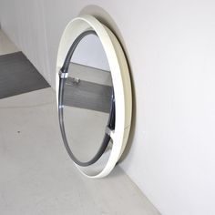 a round mirror mounted to the side of a white wall next to a gray floor