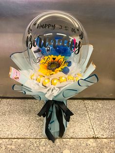 a happy birthday balloon with sunflowers and candy in it on the floor next to a wall