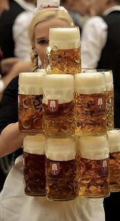 a woman in white dress carrying large mugs of beer