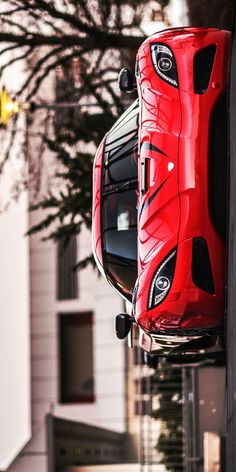 a red sports car hanging from the side of a building in front of a tree