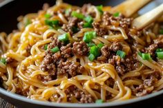 noodles with meat and green onions in a black bowl on top of a wooden table