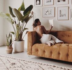 a person sitting on a couch reading a book in a room with potted plants