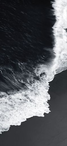 black and white photograph of the ocean with waves crashing on it's beach shore