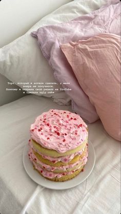 a pink cake sitting on top of a white plate next to pillows and a pillow