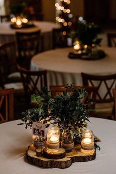 some candles are sitting on top of a wooden slab with greenery in jars and lit candles