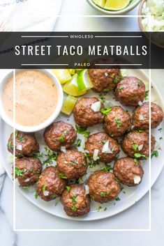 a white plate topped with meatballs next to a bowl of sauce and lemon wedges