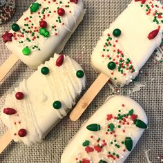 four popsicles with white frosting and candy on them sitting on a table next to christmas decorations