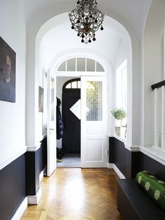 the hallway is decorated in black and white with an arched door, chandelier, and wood flooring