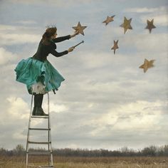 a woman in green dress standing on top of a building with stars flying above her