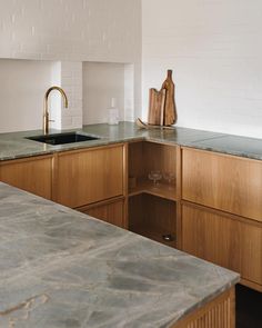 an empty kitchen with marble counter tops and wooden cabinetry, along with white brick walls