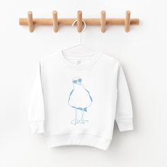 Welcome to Salty Mermaid Goods! Our mission is to bring to you whimsical and nautical designs on high quality cards, onesies, and shirts.  All of our designs are created in our Massachusetts studio and inspired by the local seashore.   Our Sal the Seagull Long Sleeve Kid's Shirt is a Rabbitskins lightweight cotton long sleeve shirt with a tear away label.  Things to know:  -Each item is handmade to order! -Please contact us to personalize a listing just for you. -Orders ship in 5-7 business days. -We carry several different brands, including Gerber, Rabbit Skins, and Bella Canvas. -Our designs are made to order, so we can not accept any returns.  But if there is a problem with your order please contact me so I can make it right. White Nautical Crew Neck Top, Nautical Cotton Tops With Graphic Print, The Seagull, Nautical Design, Long Sleeve Kids, Cotton Long Sleeve Shirt, Kids Tops, Things To Know, White Long Sleeve