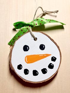 a painted snowman ornament hanging on a wood slice with a green ribbon