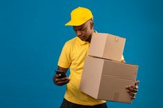 a man in a yellow shirt is holding a cardboard box and looking at his cell phone