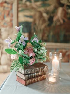 a table topped with books and flowers next to a lit candle on top of a table