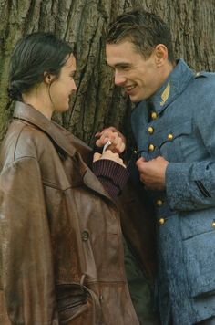 two people standing next to each other in front of a tree and one person is adjusting the jacket