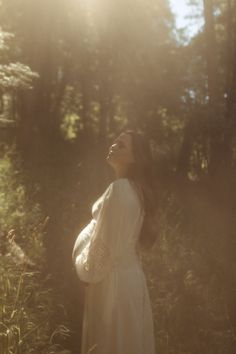 a pregnant woman standing in the woods with her eyes closed and looking up to the sky