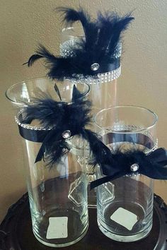 two clear vases with black feathers on top of each one are sitting on a table