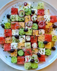 a white plate topped with cucumbers, tomatoes and olives next to other vegetables