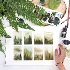 a person holding a paintbrush next to some plants and watercolors on a table