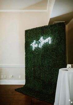 the sign is lit up in front of a wall covered with green grass and white table cloth